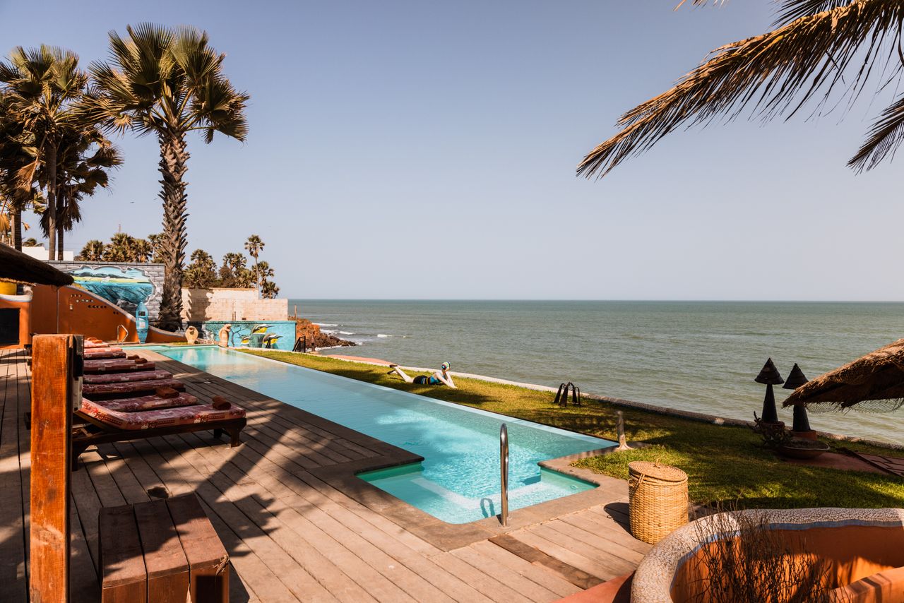 Serene coastal resort with palm trees, sunbeds, and ocean view from the pool.